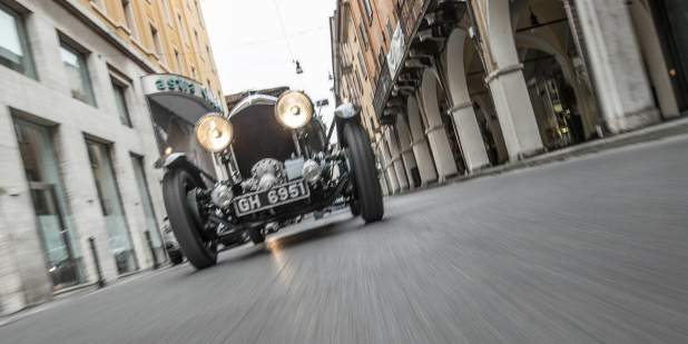 Low front view of a heritage Bentley Blower car driving past buildings | Bentley Motors