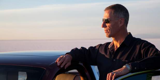 Andy Green wearing sunglasses, leaning over his Bentley and admiring the sunset  | Bentley Motors 
